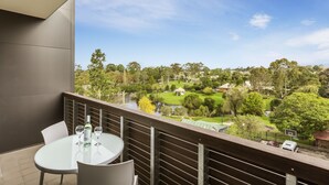 A balcony with a glass table and chairs, overlooking a park with trees and a pond. - Quest Nowra (Nowra)