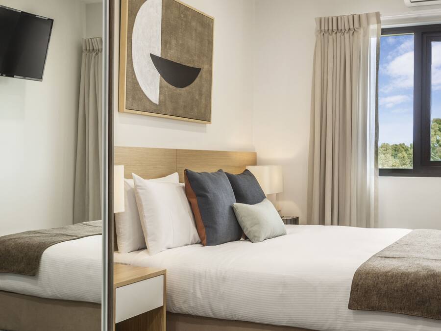 A modern hotel room with a large bed, a bedside table, a flat-screen TV, and a window with curtains.