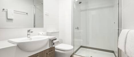 Een moderne badkamer met een douchecabine van glas, een witte wastafel en een toilet.