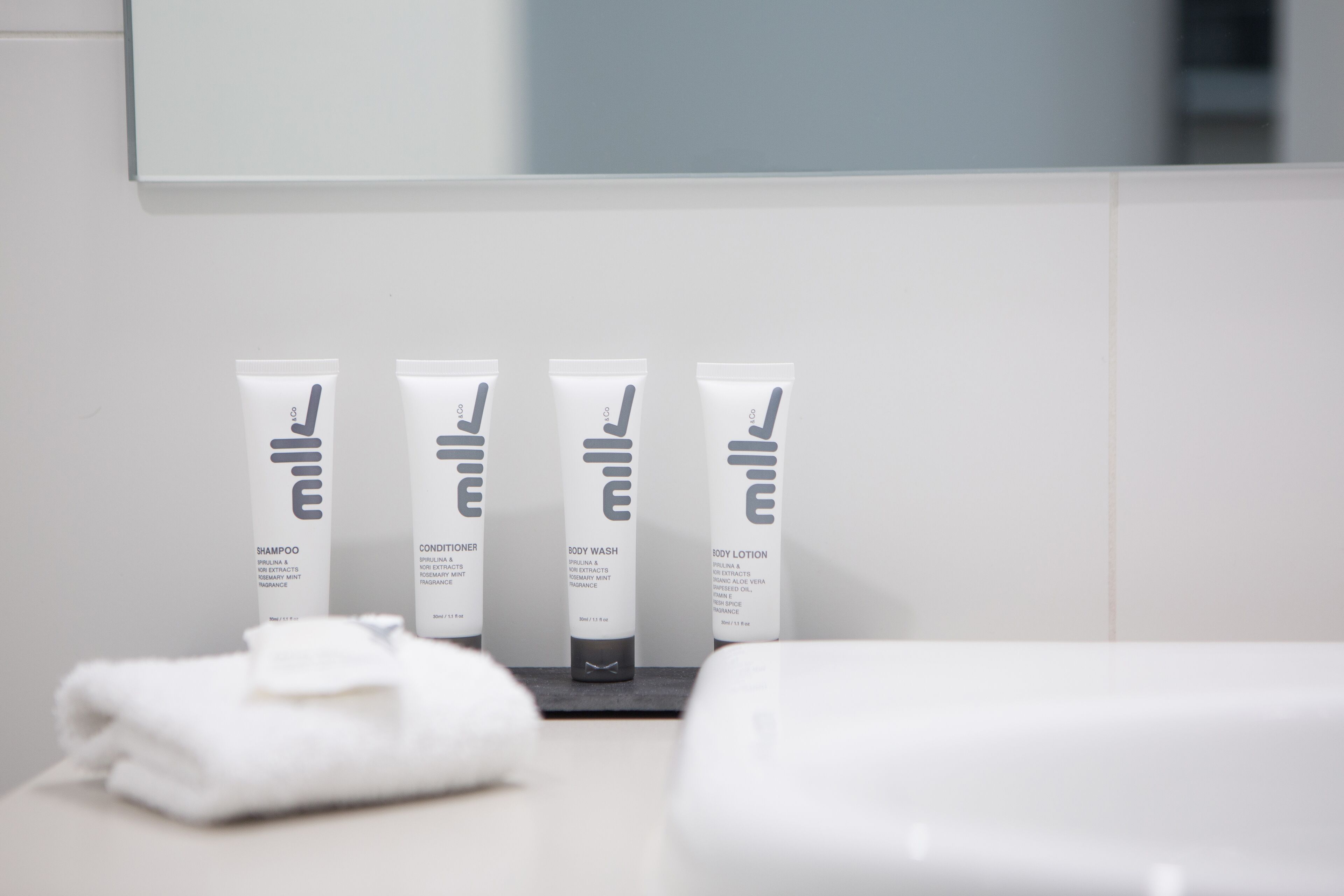 Un baño con un lavamanos blanco, un espejo y cuatro artículos de tocador: champú, acondicionador, gel de ducha y loción.