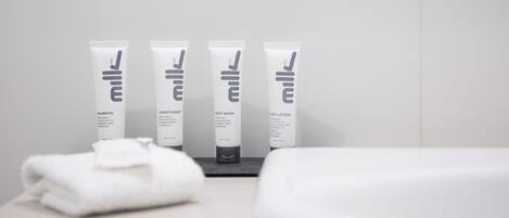 Un baño con un lavamanos blanco, un espejo y cuatro artículos de tocador: champú, acondicionador, gel de ducha y loción.