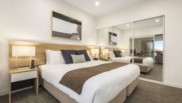 A hotel room with a large bed, a bedside table with a lamp, a mirror, and a view of the outside.