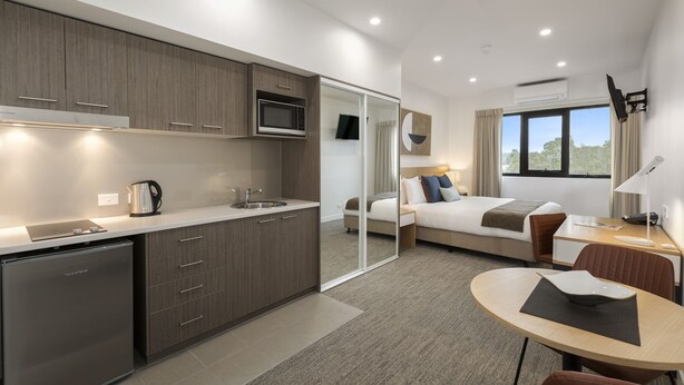 A modern hotel room with a kitchenette, a bed, a desk, and a view of the outdoors. - Quest Nowra (Nowra)