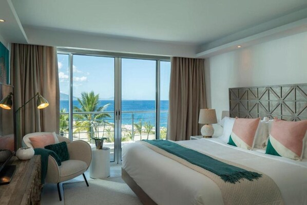 A hotel room with a large bed, a chair, a desk, and a view of the ocean. - Gansevoort Dominican Republic (Sosua)