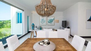 Un espace de salle à manger moderne avec une table en bois, des chaises blanches, un élément décoratif central et un grand lustre.