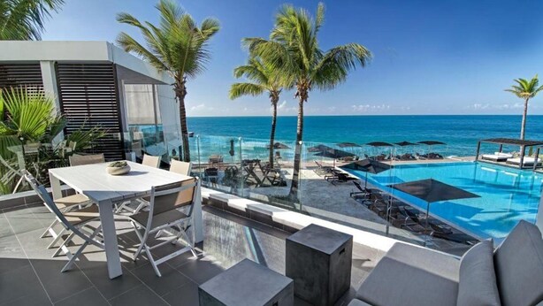 A rooftop pool area with a clear view of the ocean, palm trees, and modern outdoor furniture. - Gansevoort Dominican Republic (Sosua)
