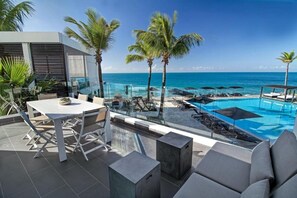 A rooftop pool area with a clear view of the ocean, palm trees, and modern outdoor furniture. - Gansevoort Dominican Republic (Sosua)