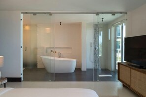 A modern bathroom with a freestanding bathtub, a glass shower enclosure, and a television on a wooden cabinet. - Gansevoort Dominican Republic (Sosua)