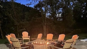 Un espacio de descanso circular al aire libre con sillas Adirondack alrededor de un brasero.