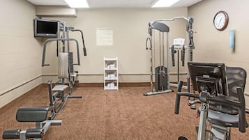 Un gimnasio con diversas máquinas de ejercicio, una televisión y un reloj en la pared.