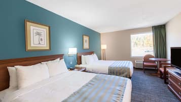 A hotel room with two beds, a desk, a chair, a television, and a window with curtains.