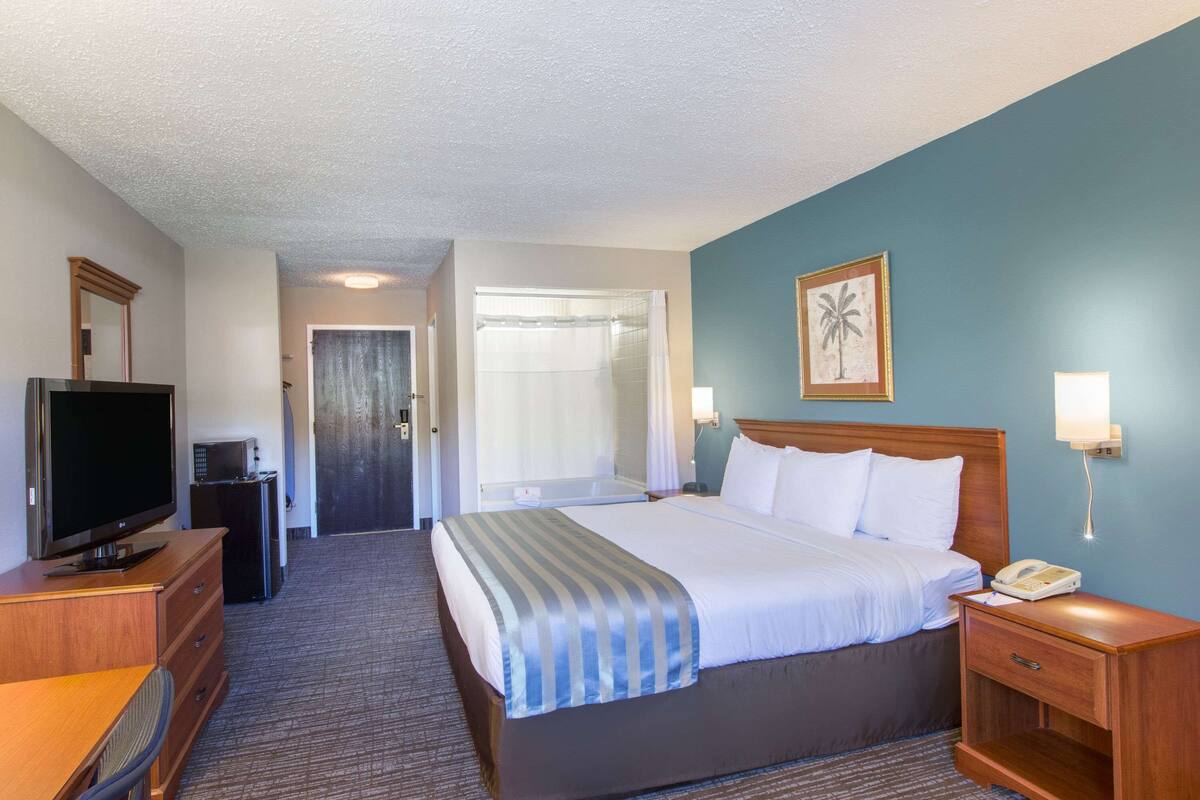 Une chambre d’hôtel comprenant un lit, un bureau avec une télévision, une table de chevet avec un téléphone et une porte donnant sur une salle de bain.