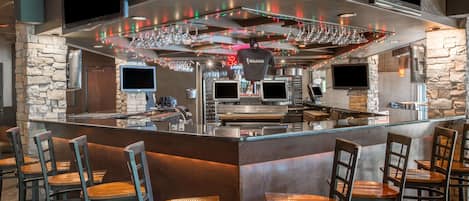 A bar area with a stone wall, bar stools, and a counter with a TV and glasses.