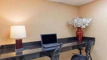 Ein Hotelzimmer mit einem Glastisch, einem Laptop, einer roten Vase mit weißen Blumen und einer Lampe.