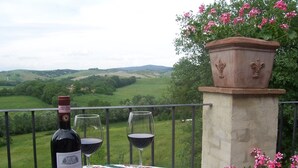 Une bouteille de vin Chianti Classico est posée sur une table, accompagnée de deux verres, et l’ensemble offre une vue panoramique sur la campagne environnante.