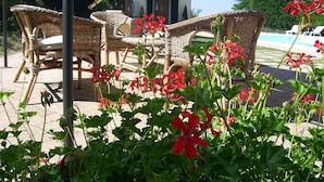Des meubles en osier, une piscine et des fleurs rouges, le tout dans un cadre extérieur ensoleillé.