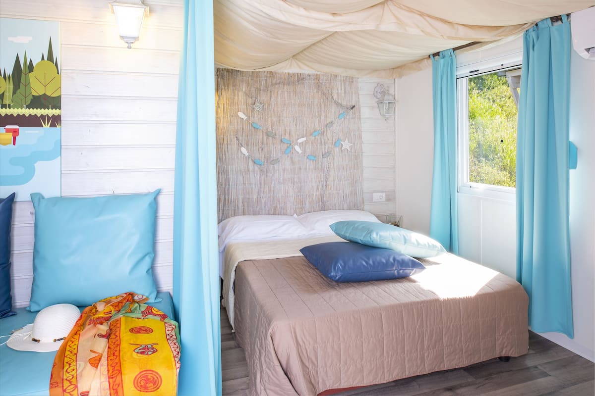 A bedroom with a bed, pillows, a headboard, a window, and curtains.