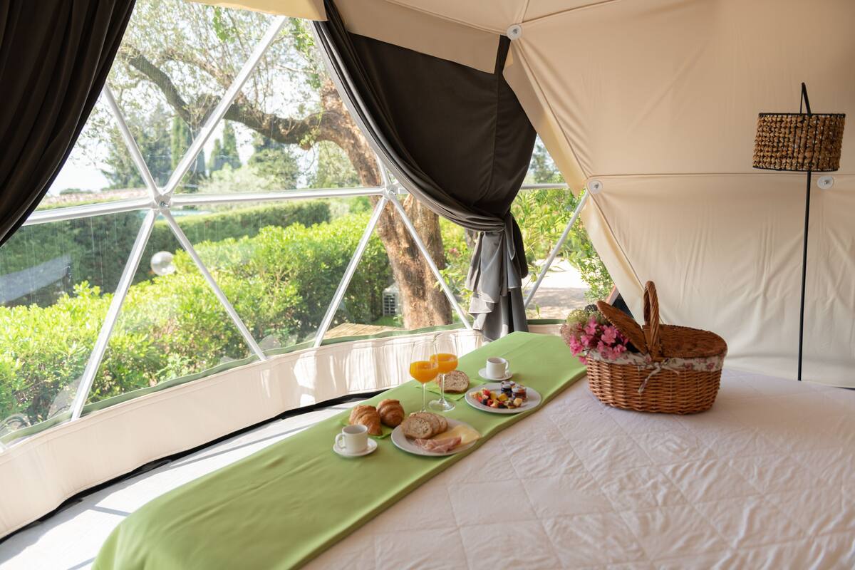 A tented room with a bed, breakfast setup, and a view of greenery outside.