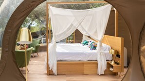 Ein Zeltraum mit einem Bett, grünen Stühlen, einer Lampe und einem kleinen Tisch.