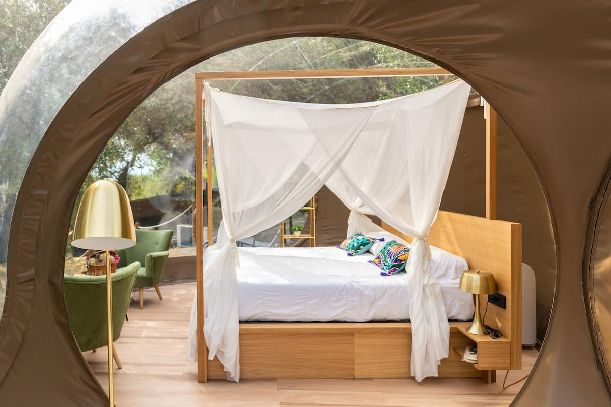A tented room with a bed, green chairs, a lamp, and a small table.