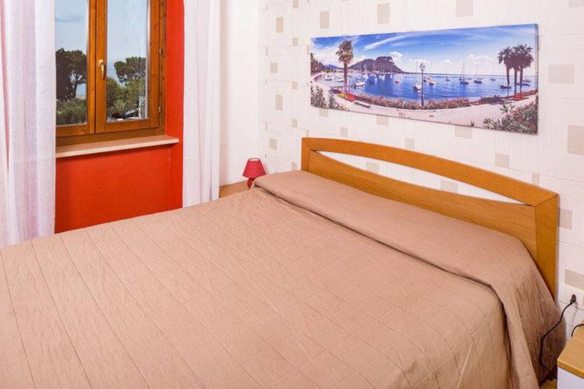 A bed with a wooden headboard, a red wall, and a window with a view of trees.