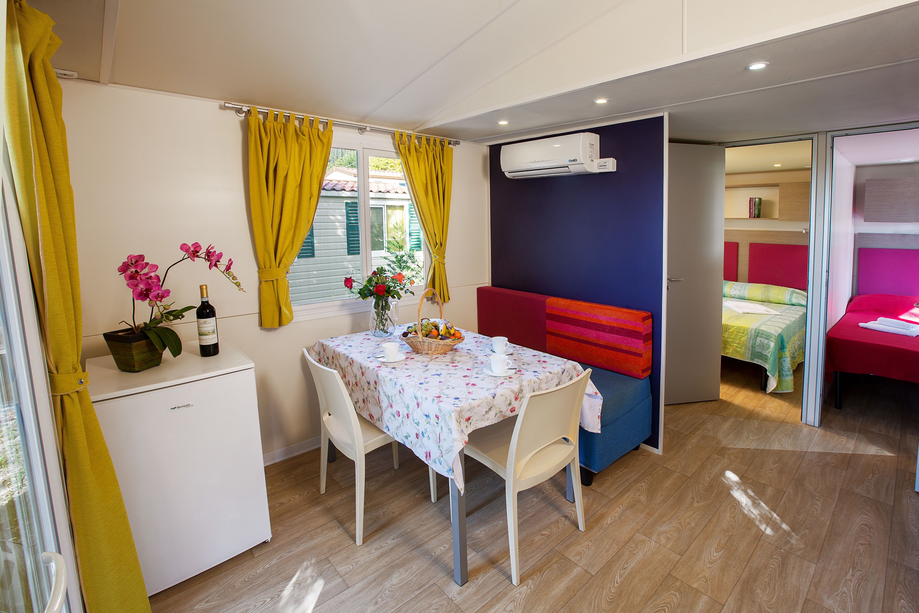 A compact room with a dining table, a small refrigerator, a sofa, and a bed.