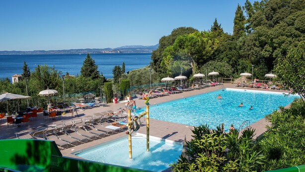 Ein Poolbereich mit Liegestühlen und Sonnenschirmen, umgeben von Bäumen und Blick auf das Meer.