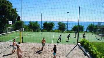 Un terrain de beach-volley avec un filet, un panier de basket et un terrain de football.