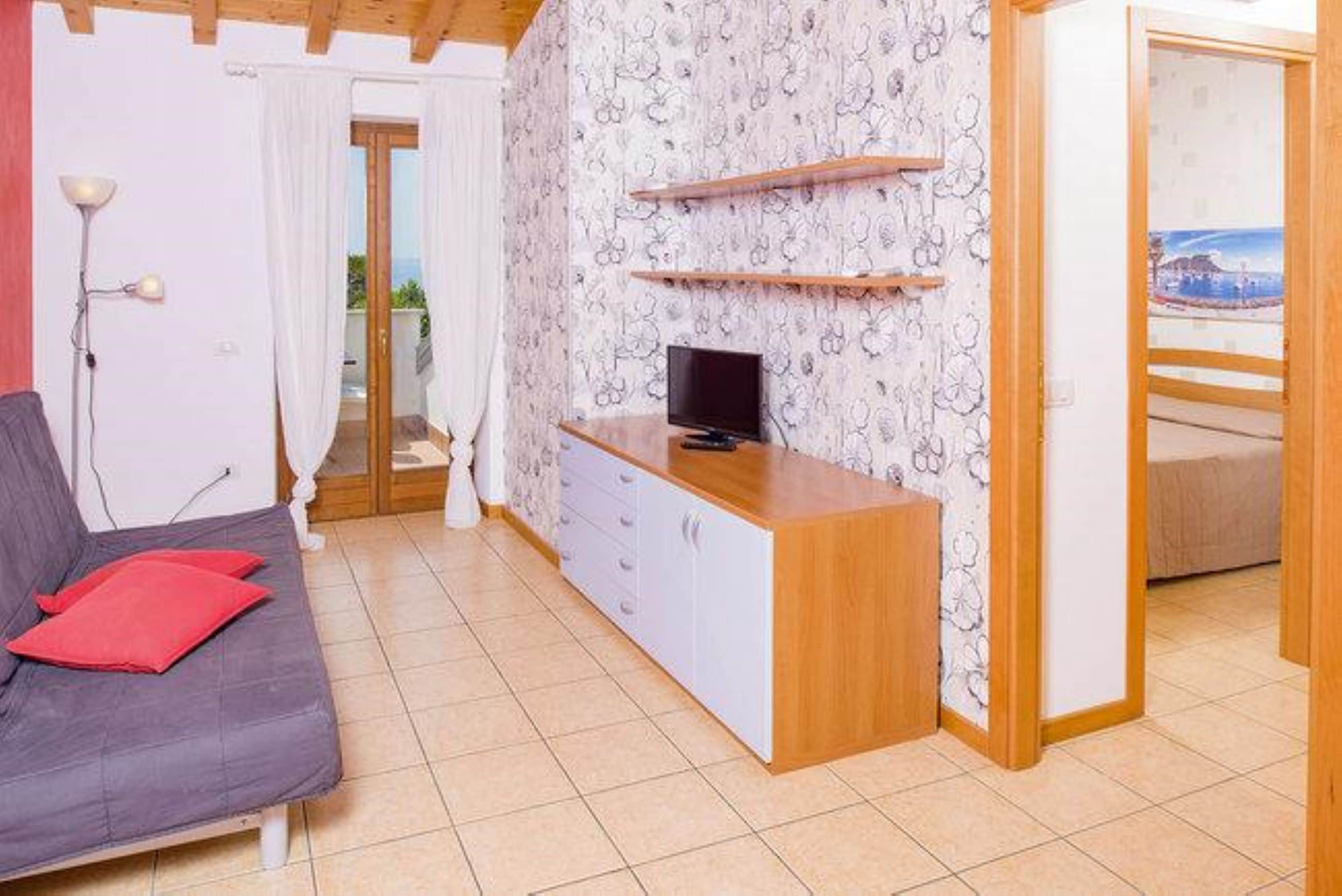 A compact living space with a grey sofa, a wooden cabinet with a television, and a patterned wallpaper.