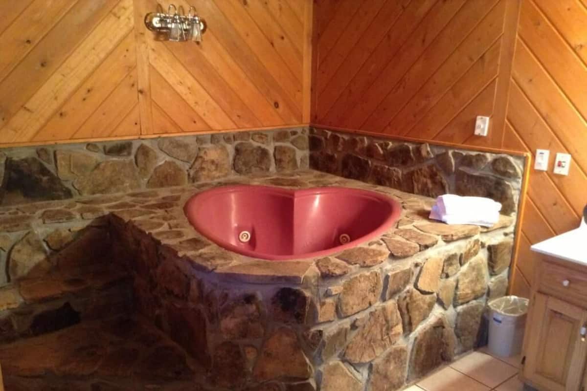 A stone bathtub with a heart-shaped design in a wooden room with stone walls.