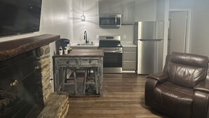 A kitchen with a stone fireplace, a wooden bar, a stainless steel refrigerator, and a leather chair. - Heidi Motel (Helen)