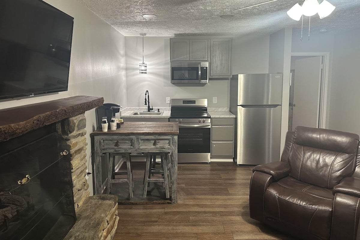A kitchen with a stone fireplace, a wooden bar, a stainless steel refrigerator, and a leather chair.