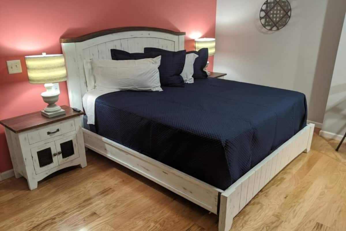A bed with a white headboard and dark blue bedding, a nightstand with a lamp, and a small cabinet.