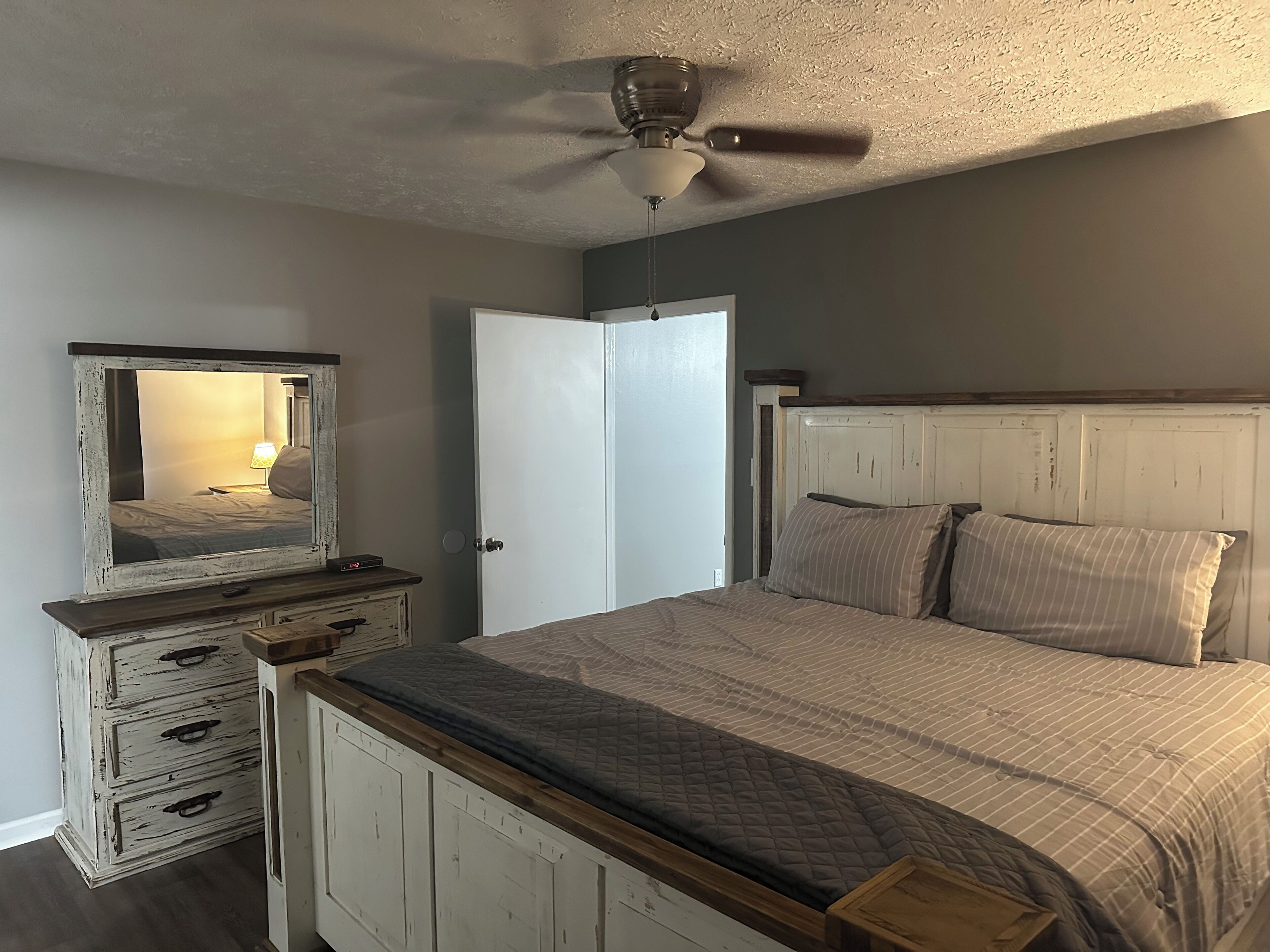 A bedroom with a bed, a dresser, a mirror, a ceiling fan, and a door.