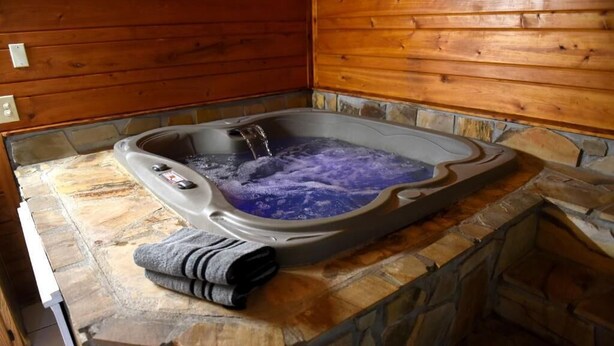 A stone-tub with a wooden interior, a control panel, and a towel on the counter. - Heidi Motel (Helen)