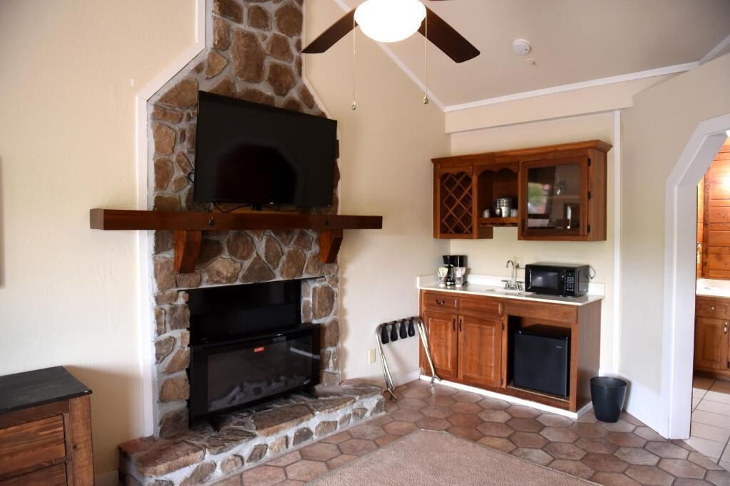 A stone fireplace with a flat-screen TV, wooden cabinets, and a kitchen area with a microwave and refrigerator.