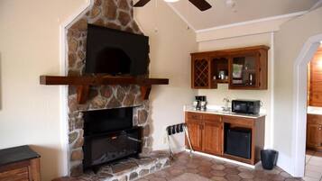 A stone fireplace with a flat-screen TV, wooden cabinets, and a kitchen area with a microwave and refrigerator.