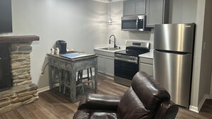 A modern kitchen with a stone fireplace, a dining table, a leather chair, and stainless steel appliances. - Heidi Motel (Helen)