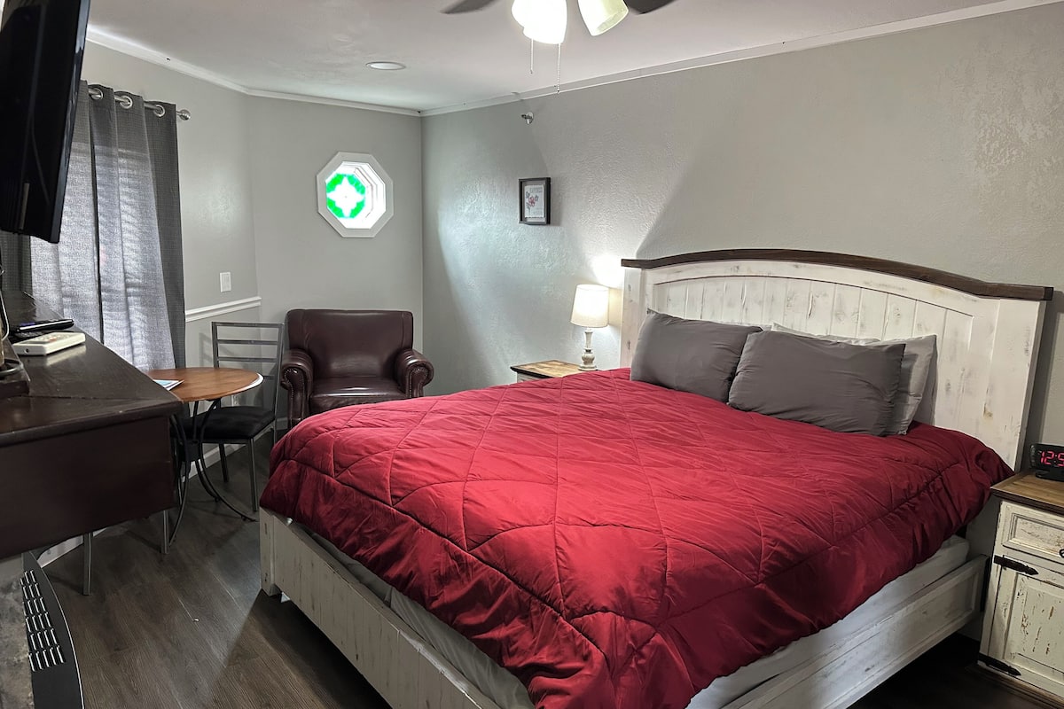 A hotel room with a bed, a desk, a chair, a nightstand, and a ceiling fan.
