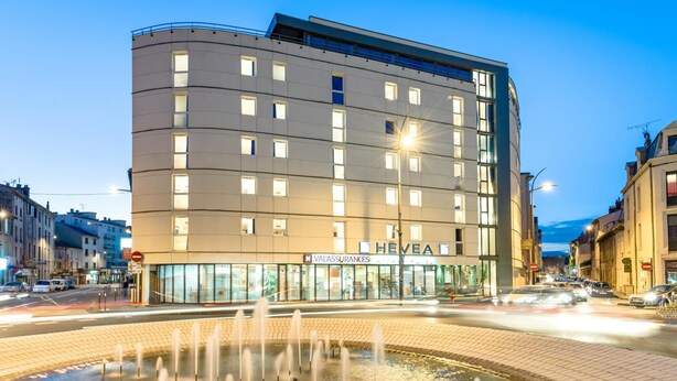 A modern hotel with a curved facade, multiple windows, and a visible sign for 'ValuAssurances'. - The Originals Residence, Appart'Hôtel Hévéa, Valence (Valence)