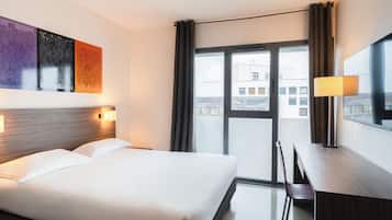 Een hotelkamer met een bed, bureau, stoel, groot raam en kunst aan de muur.