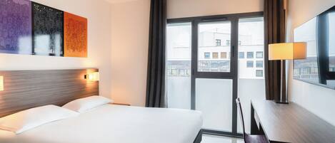 Habitación de hotel con cama, escritorio, silla, ventana grande y una obra de arte en la pared.