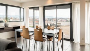 A modern dining area with a large table and chairs, large windows with curtains, and a view of the cityscape. - The Originals Residence, Appart'Hôtel Hévéa, Valence (Valence)