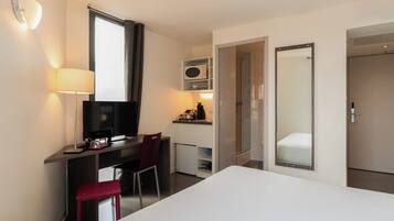 Una habitación de hotel con cama, escritorio, silla, televisor y espejo.