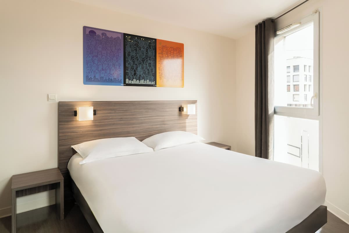 A hotel room with a bed, bedside tables, and a window with a view.