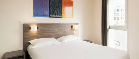 A hotel room with a bed, bedside tables, and a window with a view.