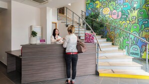 A reception desk with a modern design, a staircase with a colorful mural, and a plant on the wall. - The Originals Residence, Appart'Hôtel Hévéa, Valence (Valence)