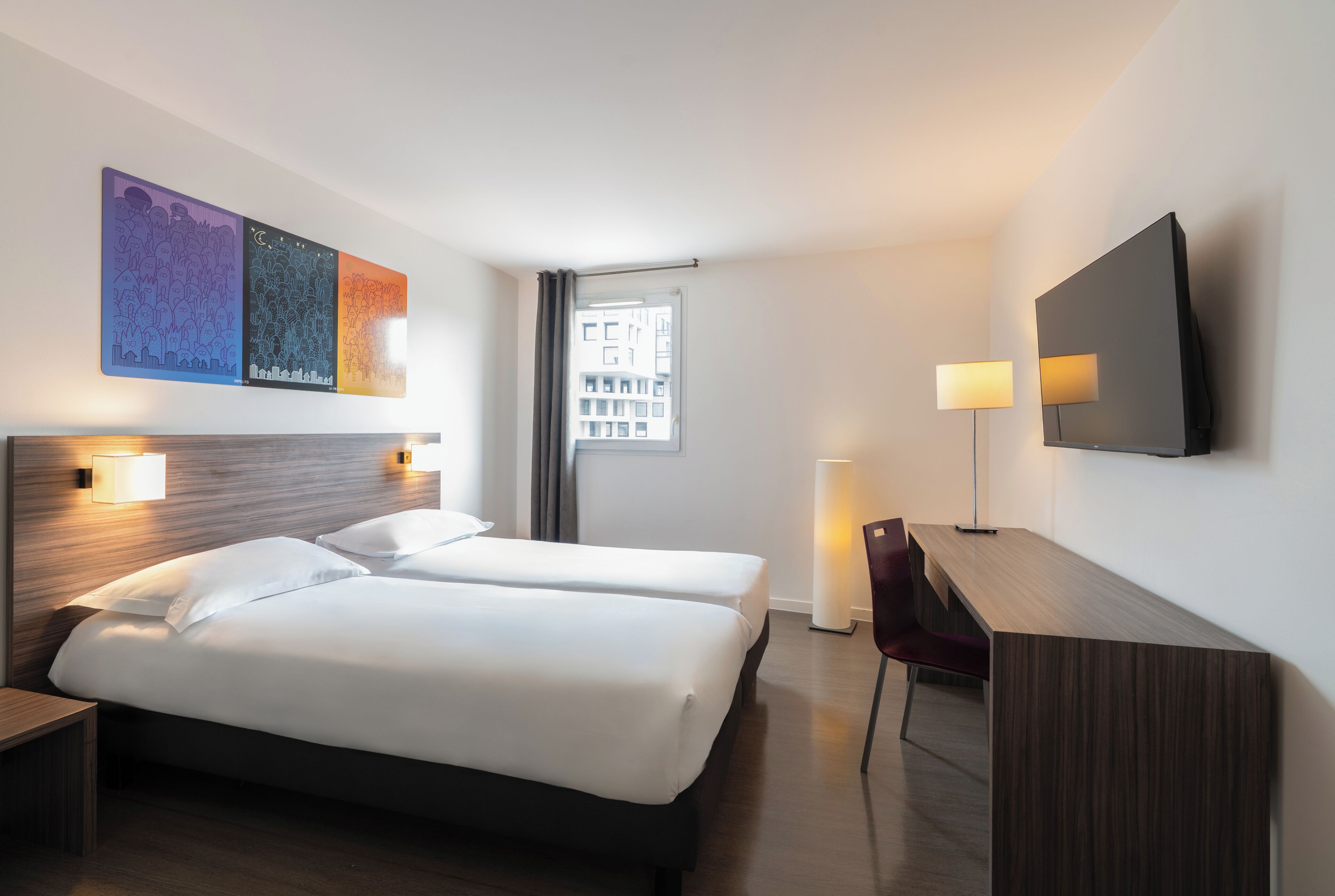 A hotel room with two beds, a desk, a chair, a TV, and artwork on the wall.
