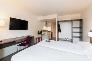 A hotel room with a bed, desk, chair, TV, closet, and kitchenette. - The Originals Residence, Appart'Hôtel Hévéa, Valence (Valence)