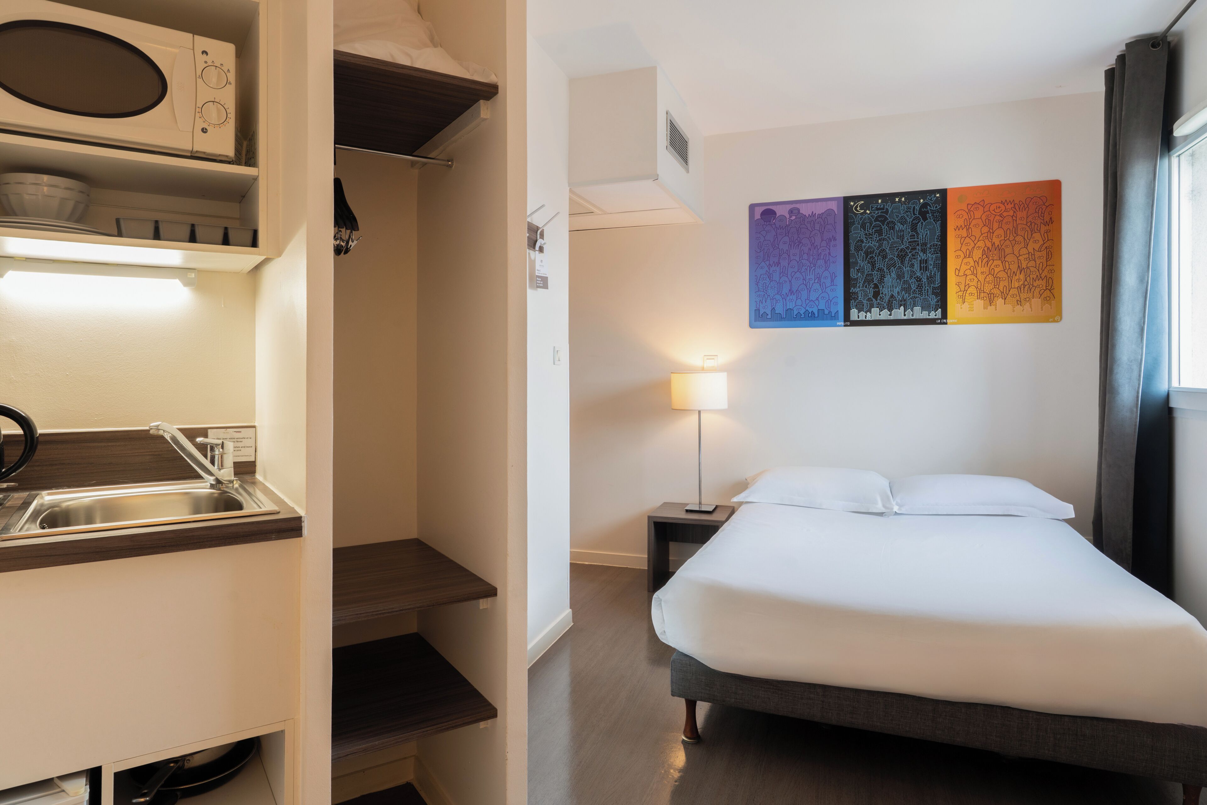 A hotel room with a bed, a nightstand, a lamp, a microwave, and a sink.